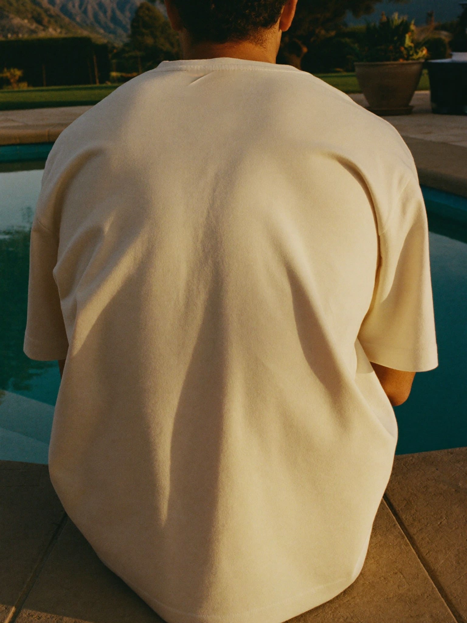 The back of the shirt, worn seated at the edge of the pool in golden light — The List prints on the front only