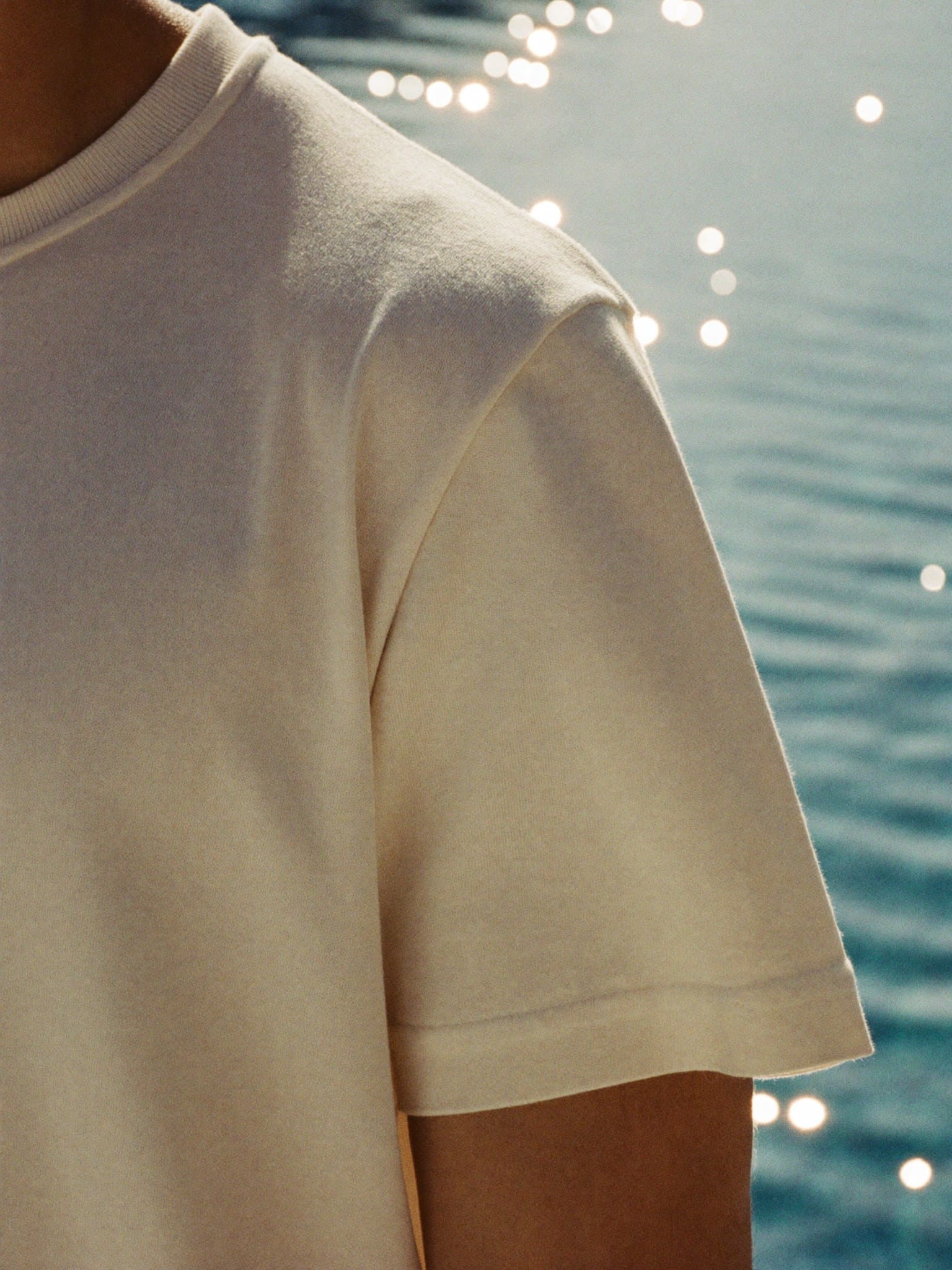 The shoulder and sleeve up close, the water of the pool soft behind the seam