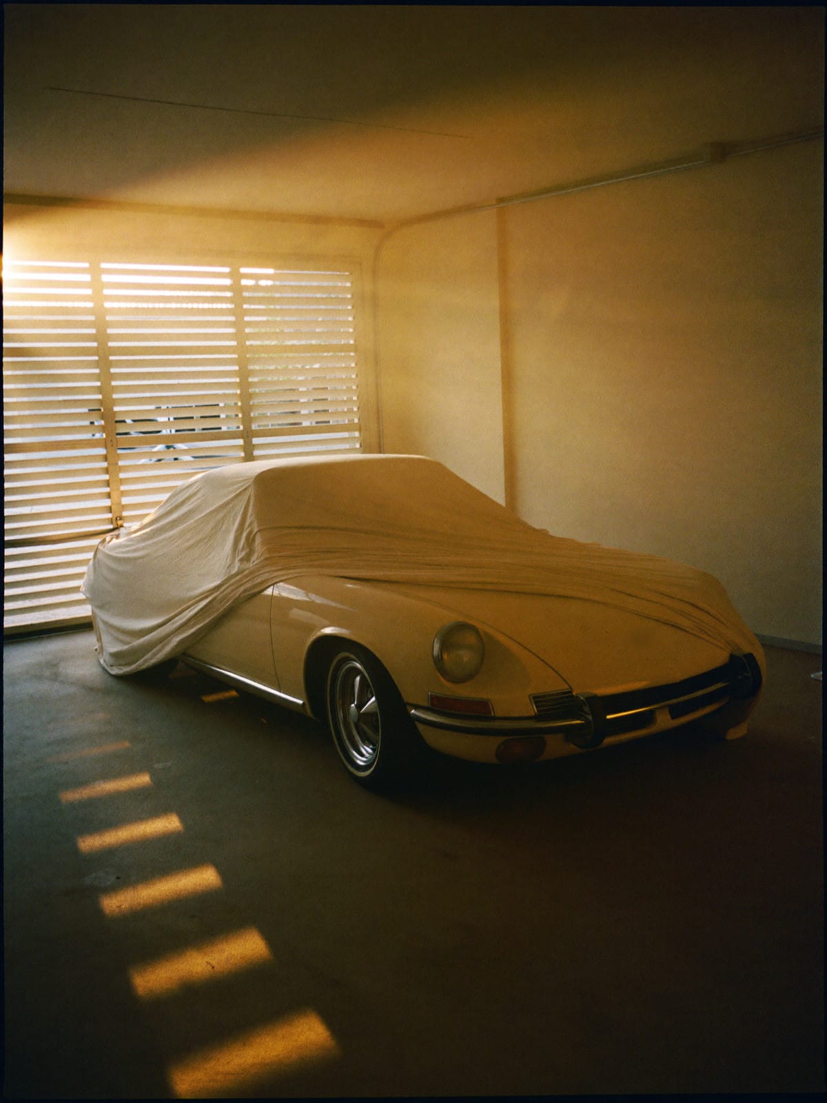 Morning garage: a car resting under a dust sheet before the light arrives.