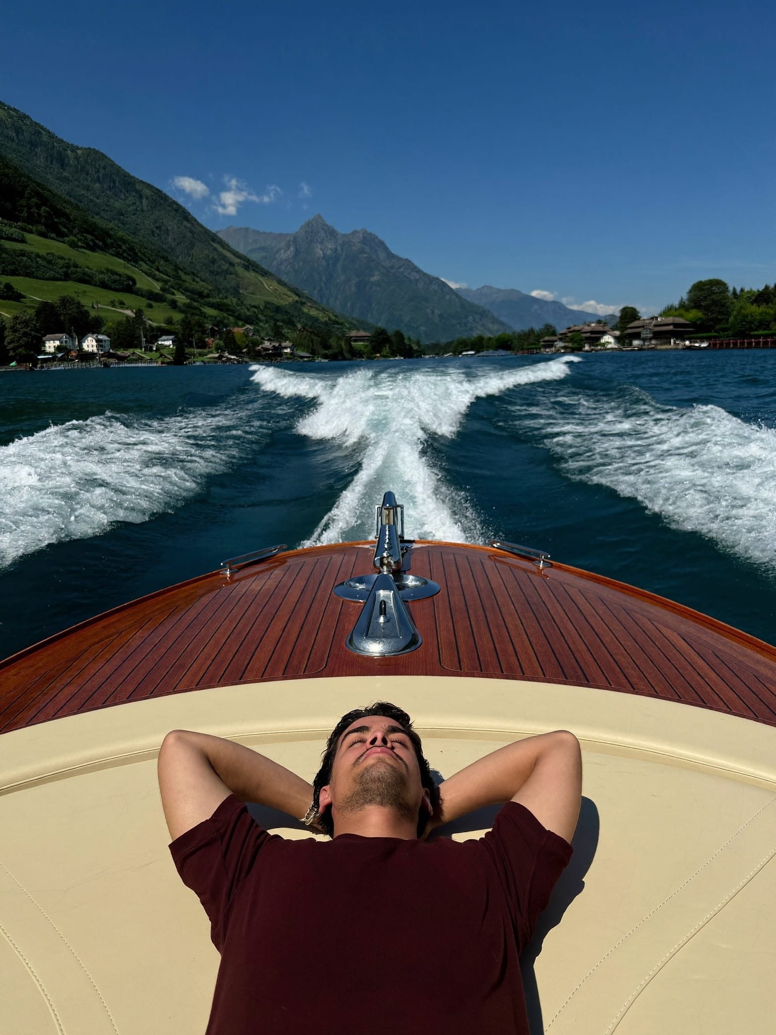 Lying back on the foredeck of a varnished mahogany runabout, twin wake opening toward the mountains