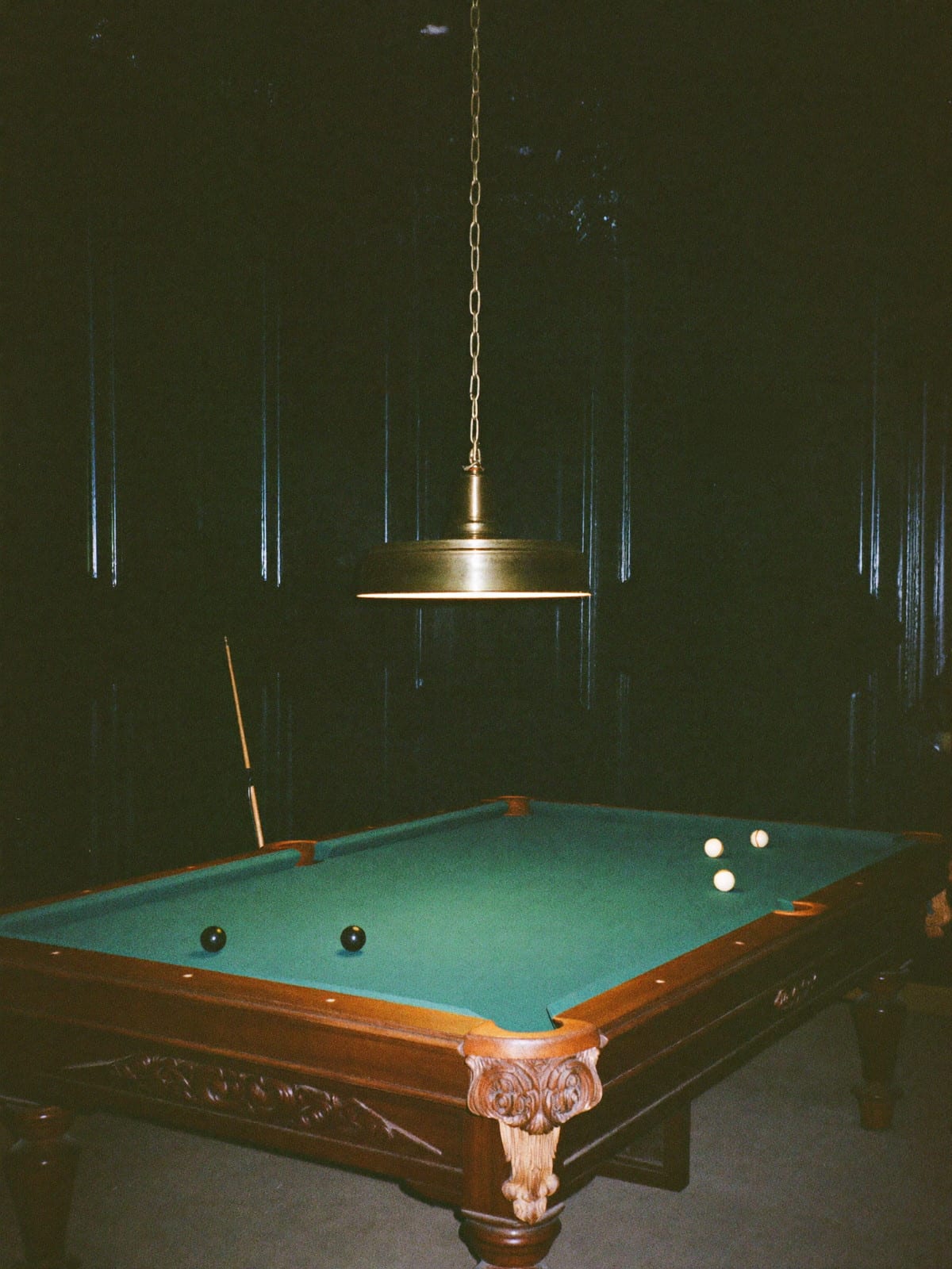 A billiard room at night, the cloth lit, the rest of the room in shadow.