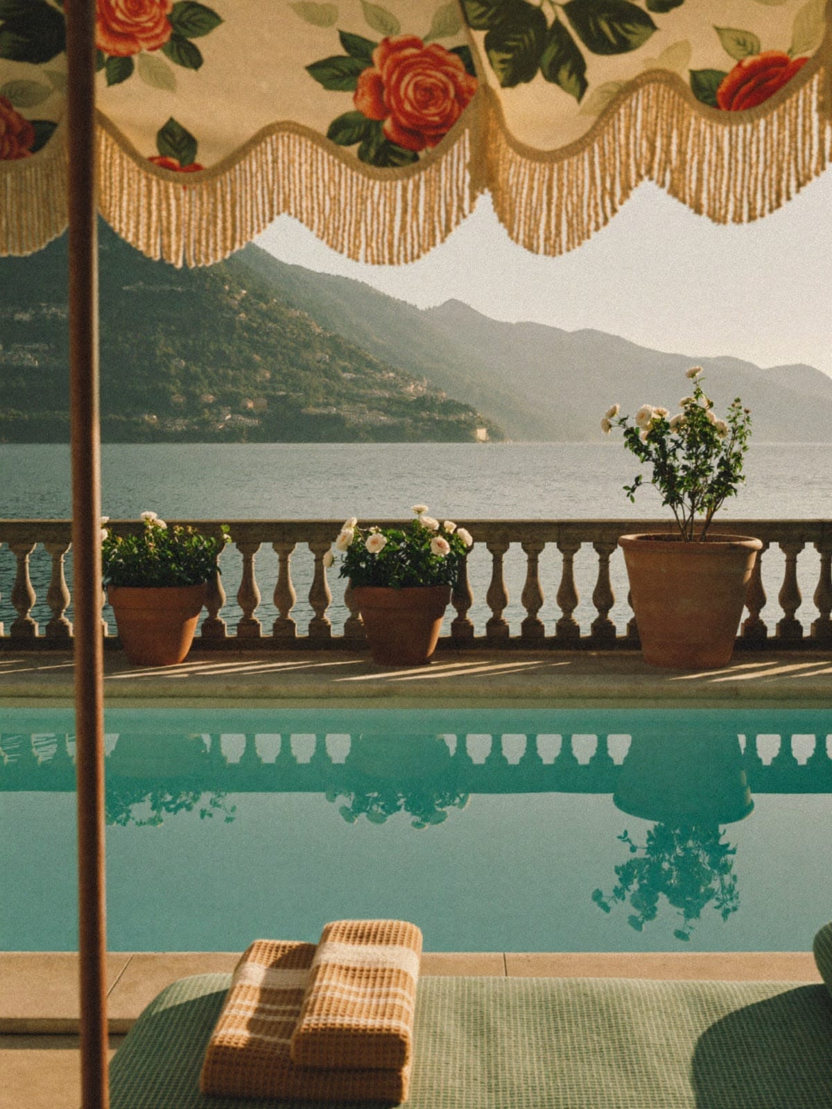 A still turquoise pool framed by a fringed parasol, the lake and the mountains beyond.
